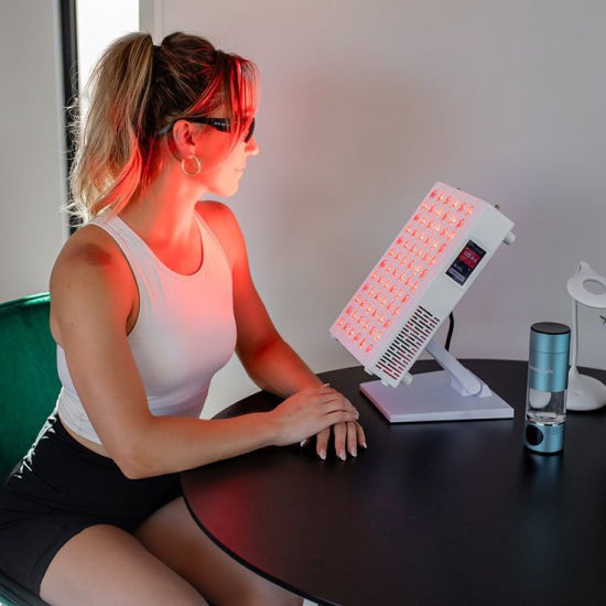 Woman receiving red light therapy from a device on a table.